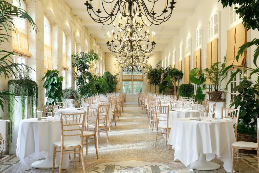 vue de la grande salle du chateau de chenonceau avec un bel éclairage blanc et chaud, de belles tables ronde, lustres et plantes