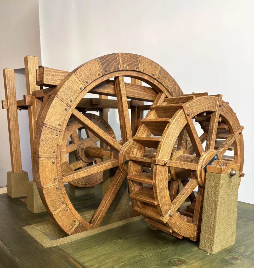 Wooden interlocking gears sculpture on a wooden platform, with riveted panels and curved wheels.
